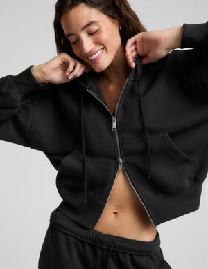 Woman wearing a black fleece zip-up sweatshirt and black sweatpants against a plain background. 