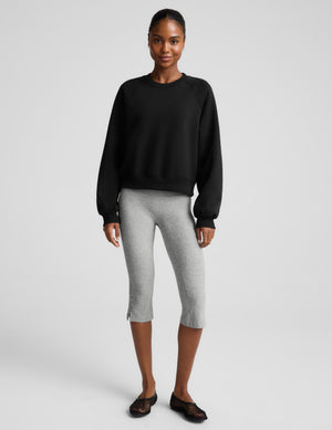 Woman wearing a black crewneck sweatshirt and gray pedal pushers against a plain background. 