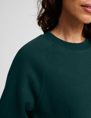 Close-up of a person wearing a dark forest green crewneck sweatshirt against a light gray background.