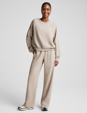 Woman wearing an oatmeal colored crewneck sweatshirt and sweatpants against a plain background. 