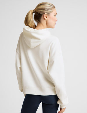 Woman wearing a white fleece hoodie and blue leggings against a plain background. 