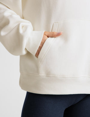 Woman wearing a white fleece hoodie and blue leggings against a plain background. 