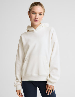 Woman wearing a white fleece hoodie and blue leggings against a plain background. 