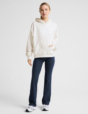 Woman wearing a white fleece hoodie and blue leggings against a plain background. 