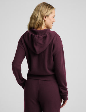 A woman modeling a matching burgundy waffle-knit zip-up hoodie and sweatpants set against a light gray studio background.