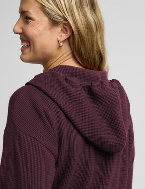 A woman modeling a matching burgundy waffle-knit zip-up hoodie and sweatpants set against a light gray studio background.