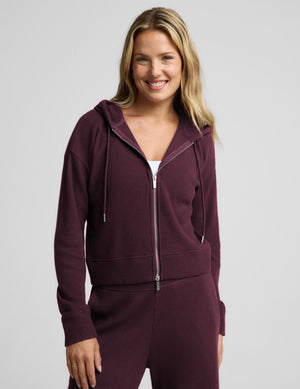 A woman modeling a matching burgundy waffle-knit zip-up hoodie and sweatpants set against a light gray studio background.