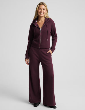 A woman modeling a matching burgundy waffle-knit zip-up hoodie and sweatpants set against a light gray studio background.