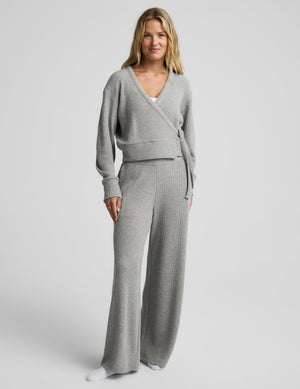 A woman modeling a light gray knit wrap cardigan and matching lounge pants against a plain light gray studio background.