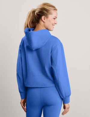 Woman wearing a blue hoodie and matching leggings against a plain studio background. 