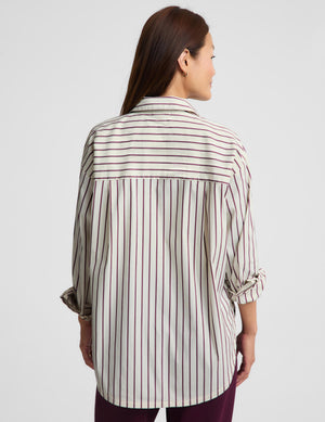 A woman shown from the back wearing a cream-colored button-up shirt with vertical stripes in dark red and thin black lines, paired with dark purple pants, against a light gray studio background.