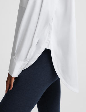 A close-up of a person wearing a loose white long-sleeve blouse and dark navy leggings against a light gray studio background.