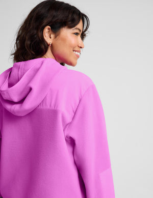 A woman shown from the back and side wearing a bright pink hooded sweatshirt against a plain light gray studio background.