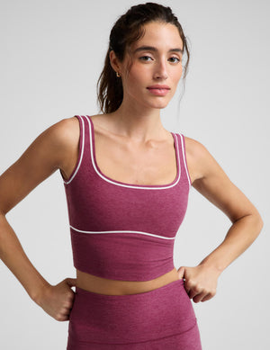 A woman modeling a matching athletic set consisting of a heathered magenta crop top and leggings with thin white contrast piping, photographed against a light gray studio background.