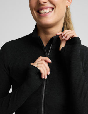 A woman modeling a black long-sleeve athletic zip top and matching black biker shorts against a light gray studio background.