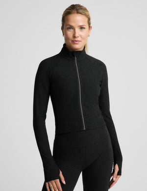 A woman modeling a black long-sleeve athletic zip top and matching black biker shorts against a light gray studio background.