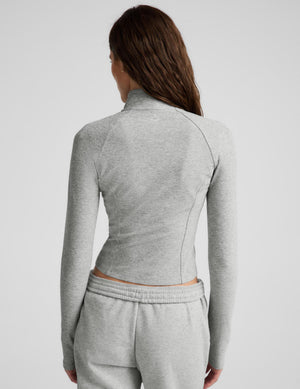 A woman modeling a light gray heather cropped zip-up athletic jacket with matching jogger sweatpants against a light gray studio background.
