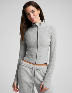 Woman wearing a gray zip-up midway length jacket and gray sweatpants against a plain background. 