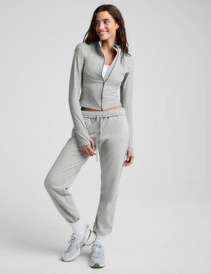 Woman wearing a gray zip-up midway length jacket and gray sweatpants against a plain background. 