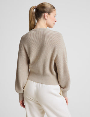 Woman wearing a neutral zip cardigan and white sweatpants against a plain background. 