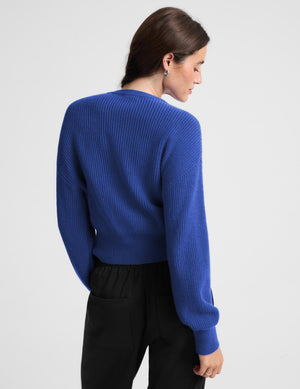 Woman wearing a blue zip cardigan and black track pants against a plain background. 