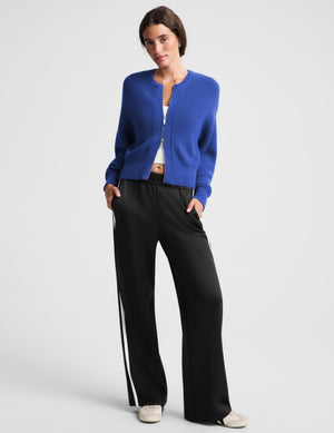 Woman wearing a blue zip cardigan and black track pants against a plain background. 