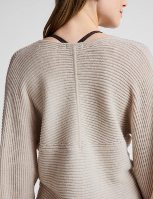 Close-up back view of a woman wearing a ribbed knit sweater in a light warm beige or oatmeal color, with dark underwire bra straps visible at the neckline.