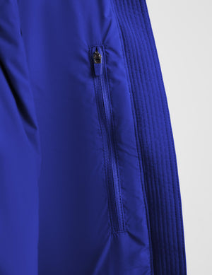 Close-up of a royal blue jacket showing a vertical zippered pocket with a small black zipper pull, alongside ribbed textured fabric panels on a light gray background.