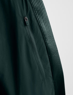 Close-up of a dark forest green jacket showing a vertical zippered pocket and a ribbed knit sleeve panel against a light gray background.