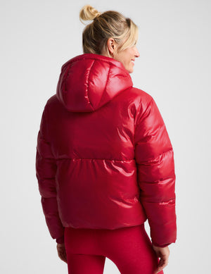 A woman shown from the back wearing a shiny red puffer jacket and matching red leggings against a light gray studio background.