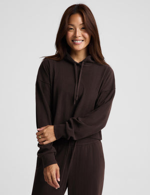 A woman modeling a dark brown ribbed knit hoodie and matching pants against a light gray studio background.