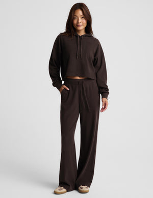 A woman modeling a dark brown ribbed knit hoodie and matching pants against a light gray studio background.