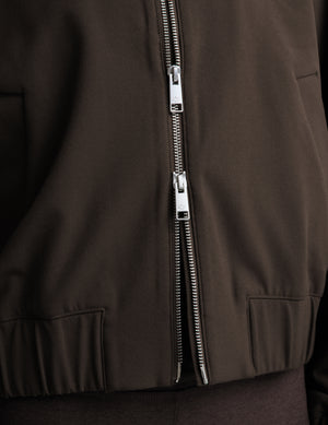 A woman modeling a dark brown zip-up jacket, matching dark brown cropped leggings, a white top, and black sneakers against a light gray studio background.