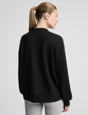 A woman modeling a black long-sleeve V-neck sweatshirt over a light gray tank top and heather gray leggings, photographed against a plain light gray studio background.