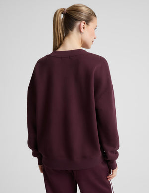 A woman wearing a matching deep burgundy lounge set, featuring a long-sleeve V-neck sweatshirt and pants. 