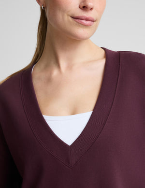 A woman wearing a matching deep burgundy lounge set, featuring a long-sleeve V-neck sweatshirt and pants. 