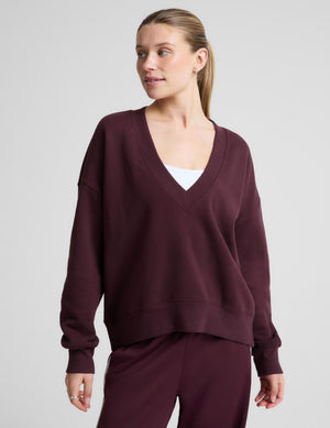 A woman wearing a matching deep burgundy lounge set, featuring a long-sleeve V-neck sweatshirt and pants. 