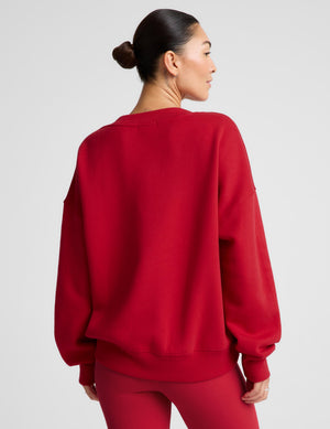 A woman shown from the back wearing a red crewneck sweatshirt and matching red leggings against a light gray studio background.