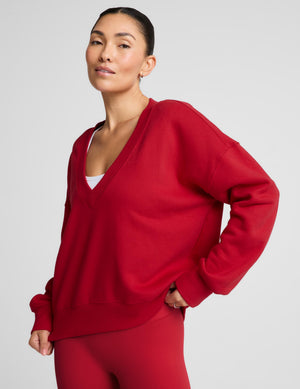 A woman modeling an oversized red V-neck sweatshirt and matching red leggings against a light gray studio background.