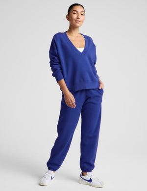A woman modeling a matching royal blue sweatshirt and jogger pants set, paired with white sneakers, against a light gray studio background.