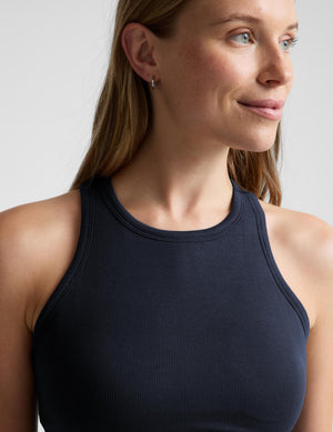 A close-up of a woman wearing a dark navy ribbed athletic tank top against a light gray background.