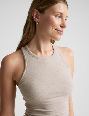 A woman wearing a ribbed knit halter tank top in a light taupe-beige color, shown from the chest up against a plain light gray studio background.