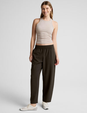A woman modeling dark olive green wide-leg pants with a matching ribbed waistband, paired with a beige ribbed crop top and white sneakers, against a light gray studio background.