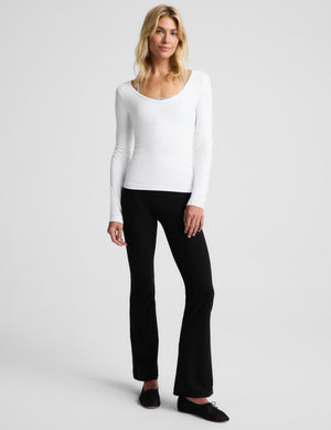 A blonde woman modeling a white long-sleeve scoop-neck top against a light gray studio background.