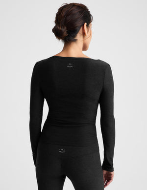 A woman modeling a black long-sleeve scoop-neck knit top and matching leggings against a light gray studio background.
