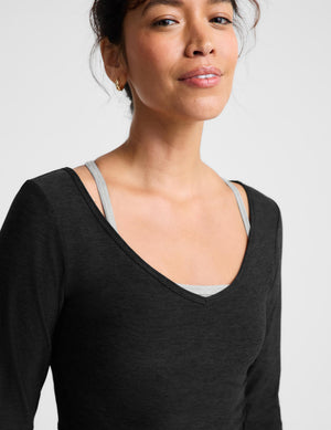 A woman modeling a black long-sleeve scoop-neck knit top and matching leggings against a light gray studio background.