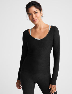 A woman modeling a black long-sleeve scoop-neck knit top and matching leggings against a light gray studio background.
