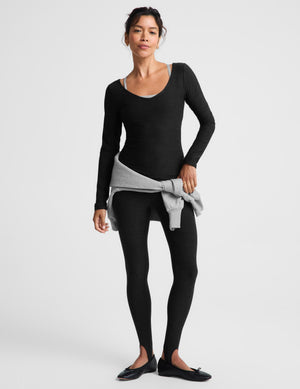 A woman modeling a black long-sleeve scoop-neck knit top and matching leggings against a light gray studio background.
