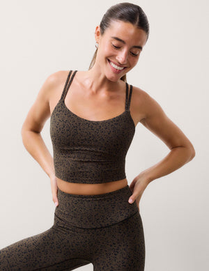 A woman modeling a matching activewear set consisting of a dark brown and black speckled sports bra and high-waisted leggings, posing against a light beige studio background.