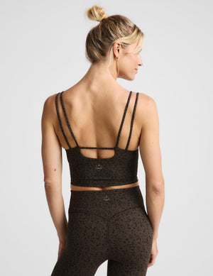 A woman shown from the back wearing a brown spotted strappy cropped tank and matching high-waisted leggings with a small leopard print, against a light gray studio background.